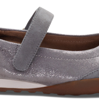 A single women's Mary Jane flat shoe in a metallic silver-gray suede-like material, featuring a hook-and-loop strap closure, a white midsole, and a brown outsole.