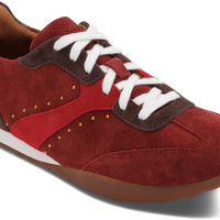 A low-top sneaker in red suede and fabric with dark brown suede overlays, white laces, and gold-tone decorative studs, shown on a white background.