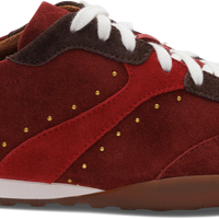 A red suede and leather sneaker with white laces, a white midsole stripe, brown heel and toe accents, and small gold stud details, shown from a side profile on a white background.