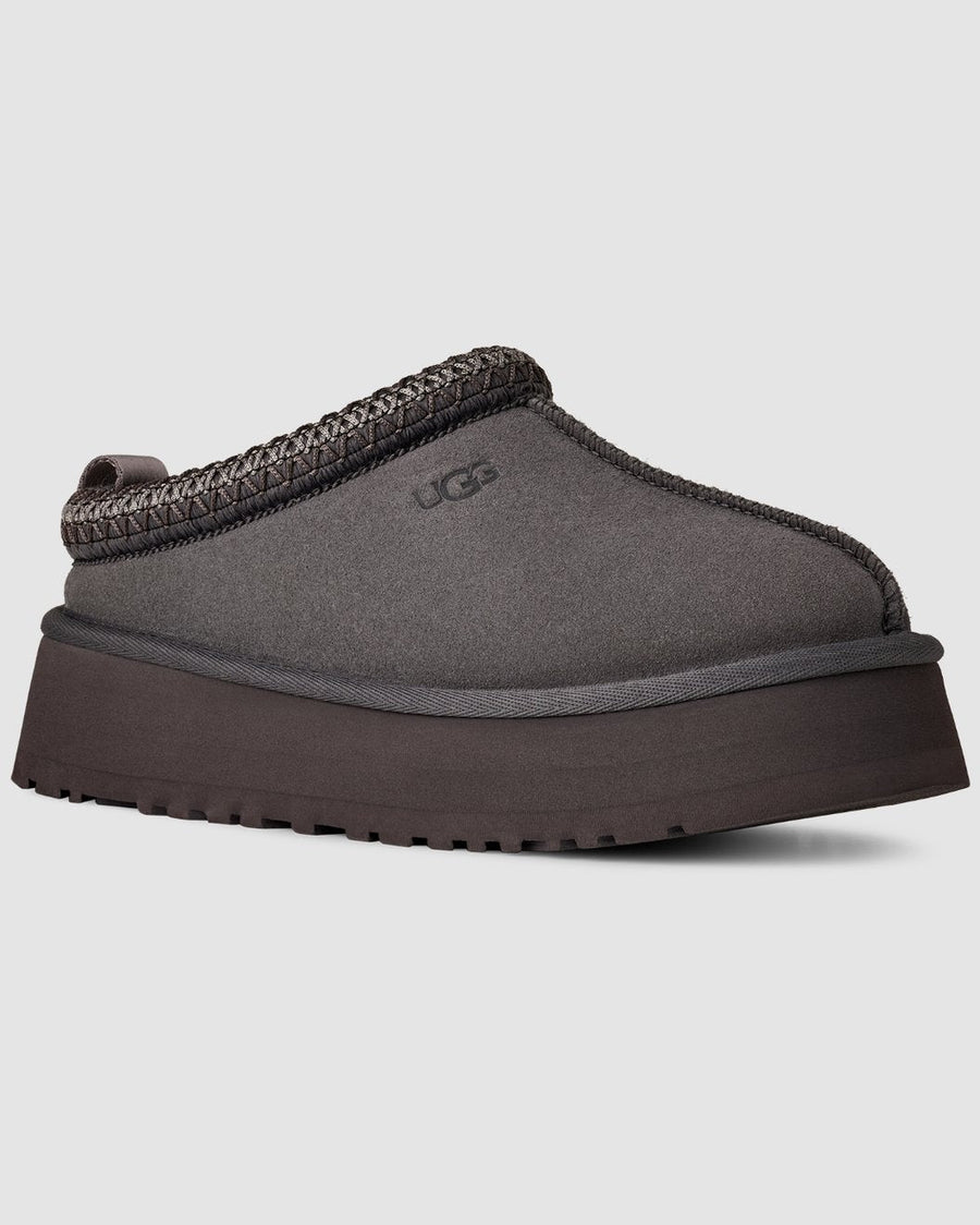 Gray UGG slipper with brown trim on a light gray background