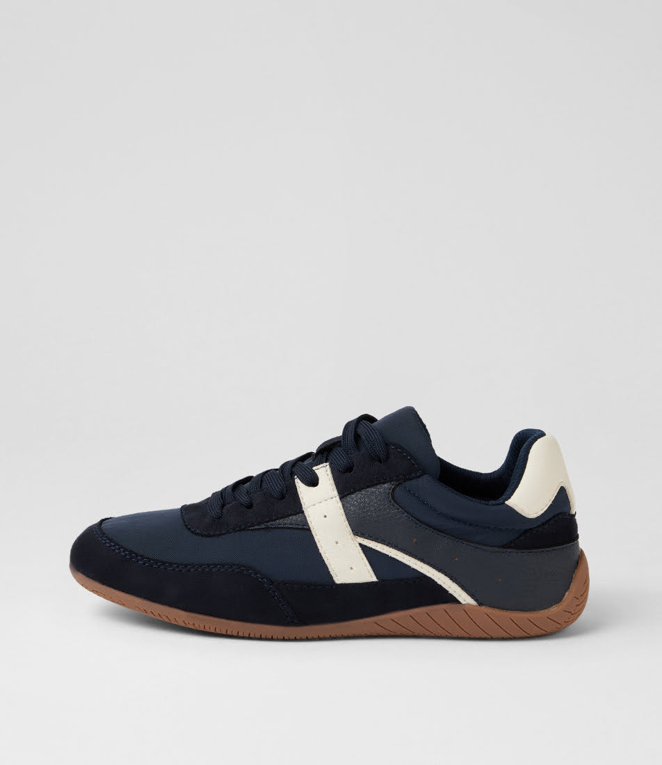 A low-top sneaker in navy blue suede and mesh with a contrasting off-white side stripe, navy heel tab, and a brown gum sole, shown from a side profile on a light gray background.