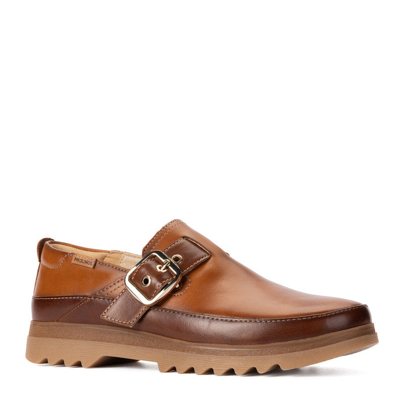A brown leather mule shoe with a double strap design, featuring a silver-tone buckle and a chunky lug sole, shown against a plain white background.